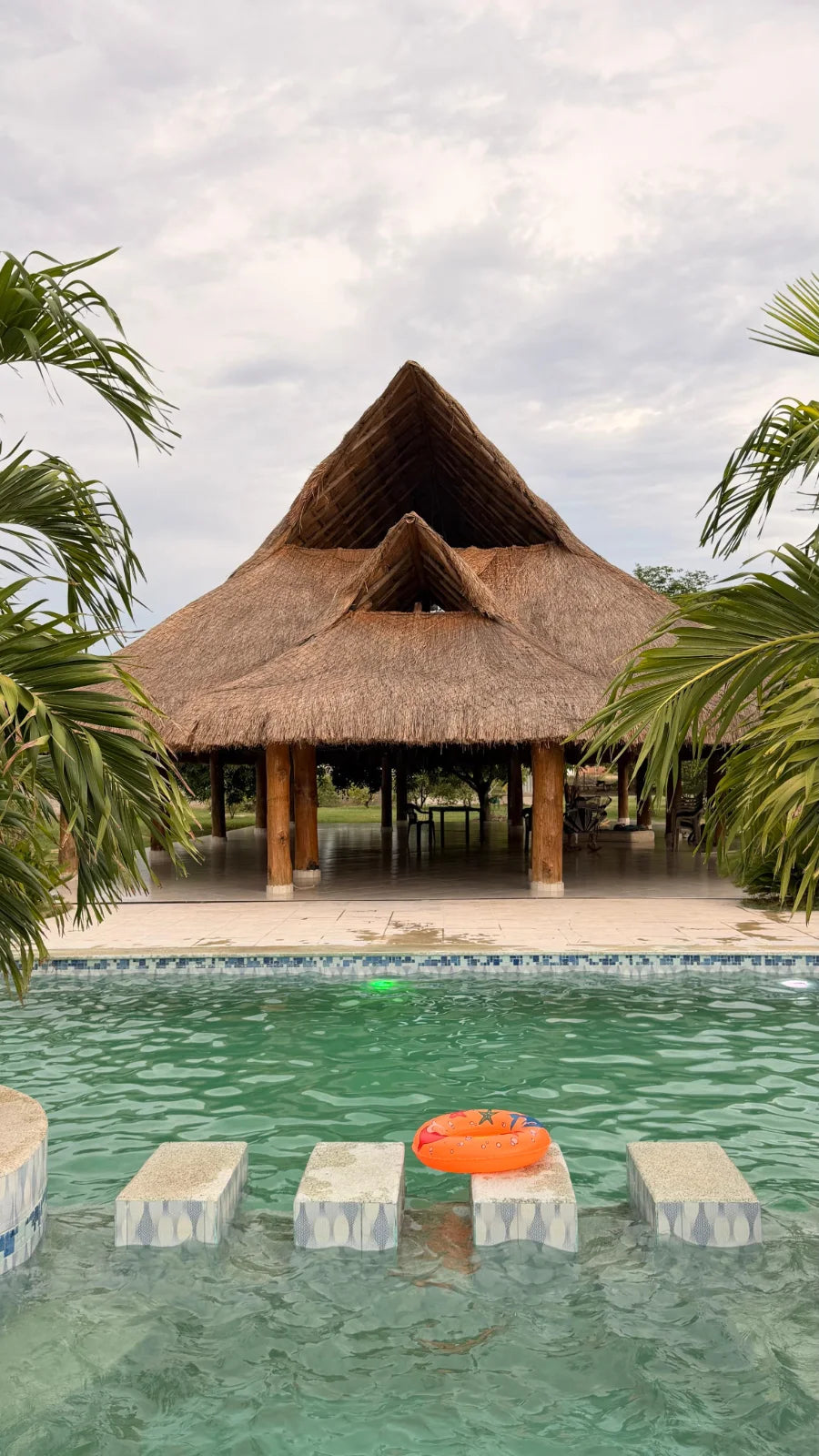 Kiosco de palma y madera frente a la piscina, enmarcado por palmeras.