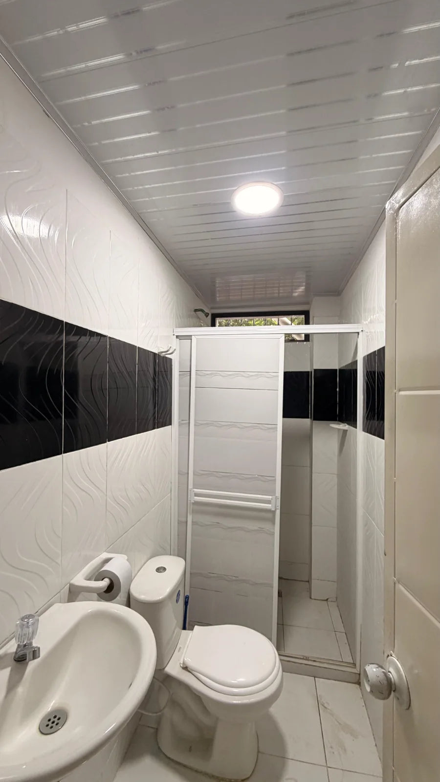 Baño con lavamanos, inodoro y ducha con división corrediza blanca.