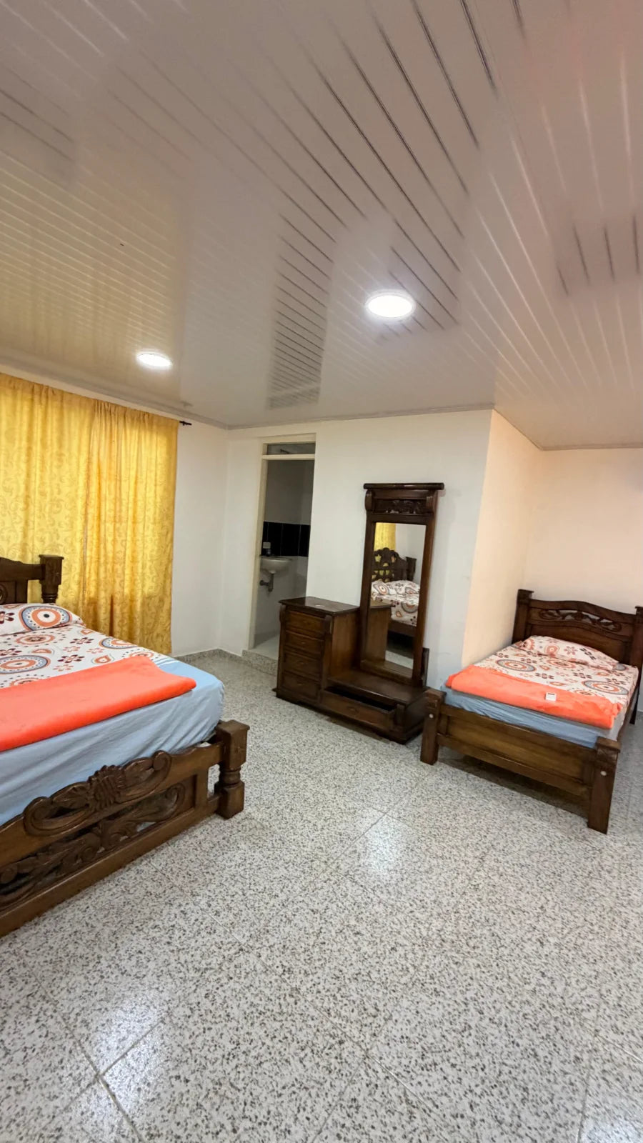 Dormitorio con camas de madera marrón, tocador y una abertura hacia un baño.
