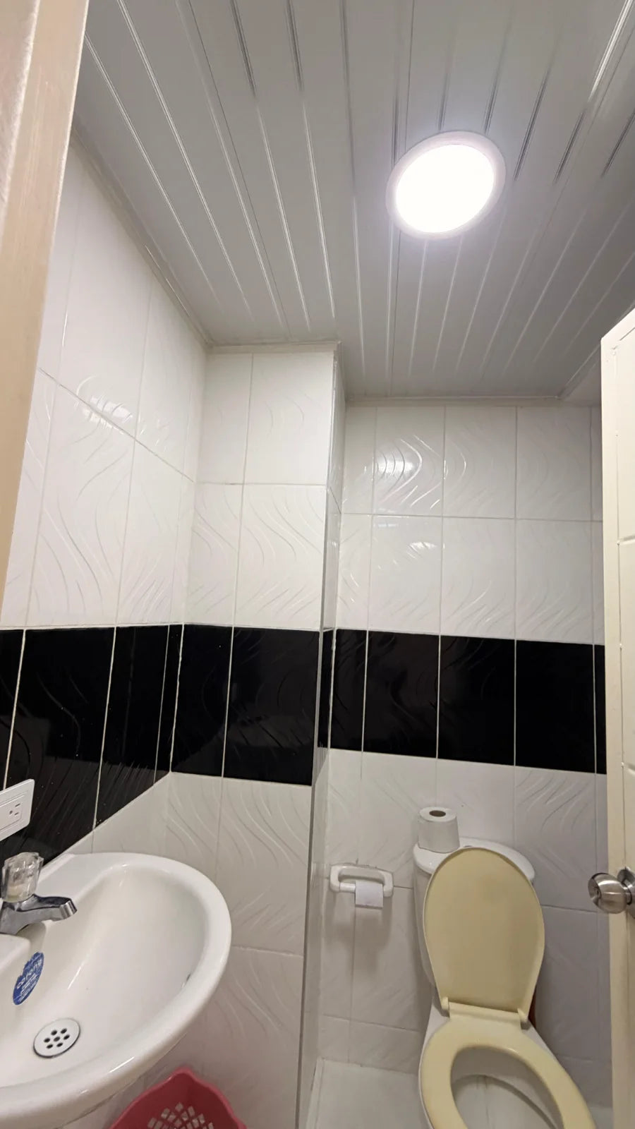 Baño de cerámica blanca y negra con lavamanos, espejo e inodoro.