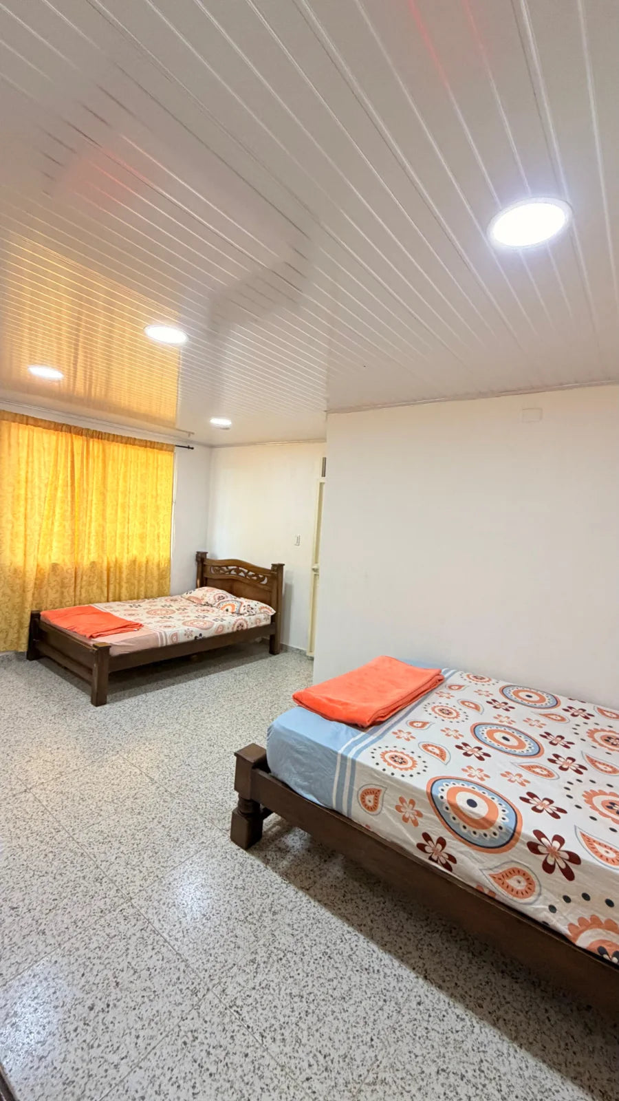 Vista longitudinal de un dormitorio de camas de madera y cortinas amarillas.