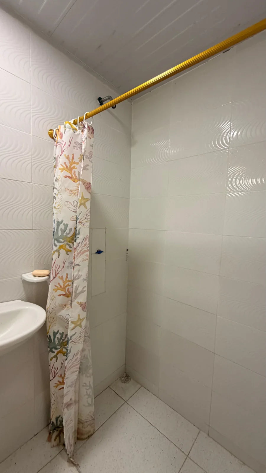 Ducha con cortina estampada y paredes de cerámica blanca.