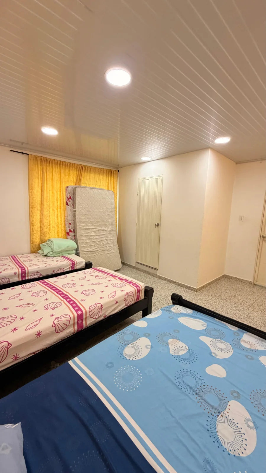 Vista del dormitorio de camas negras hacia puertas blancas y cortinas amarillas.