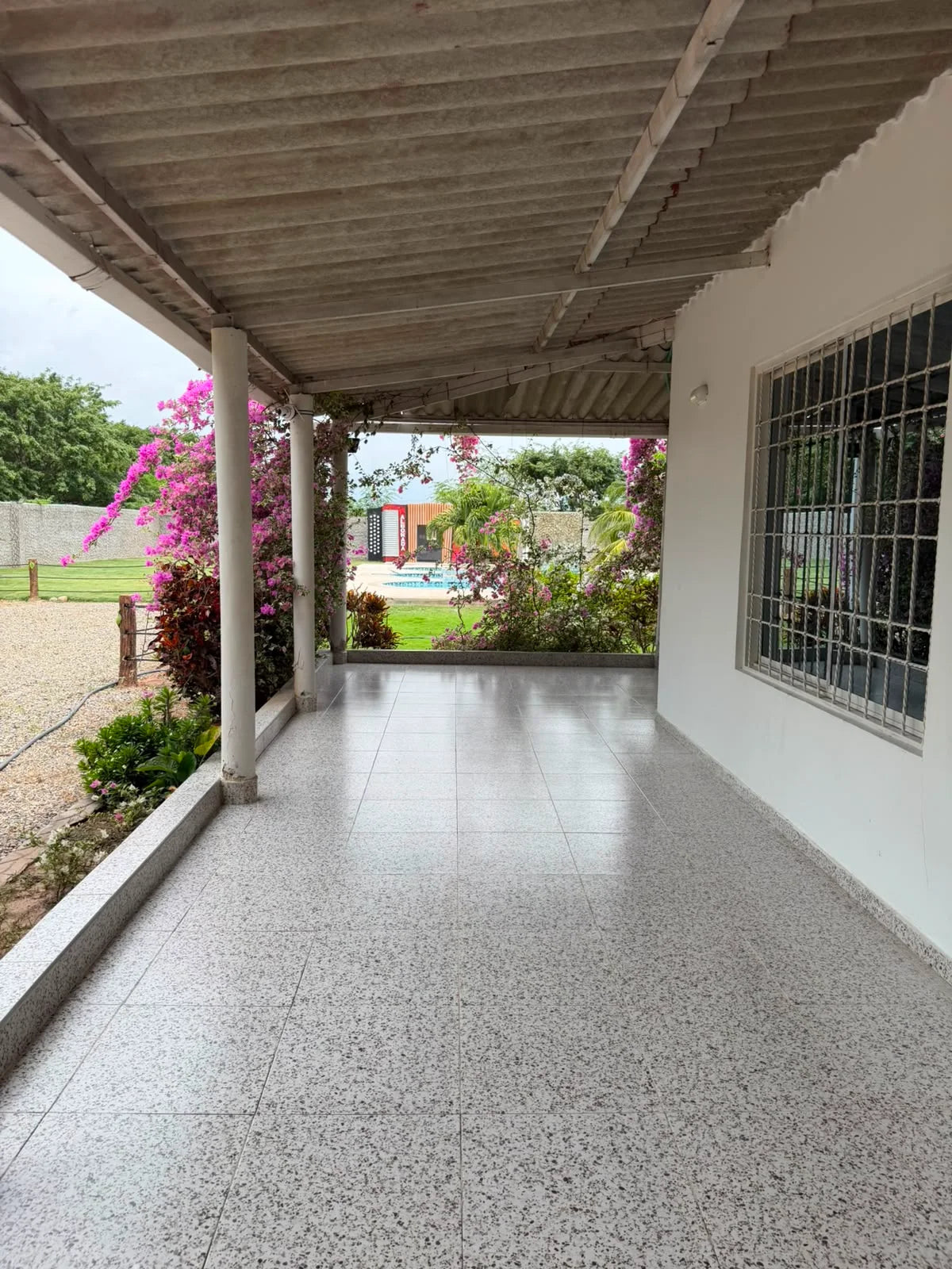 Corredor cubierto de la casa con columnas blancas y vista hacia el jardín y la piscina.