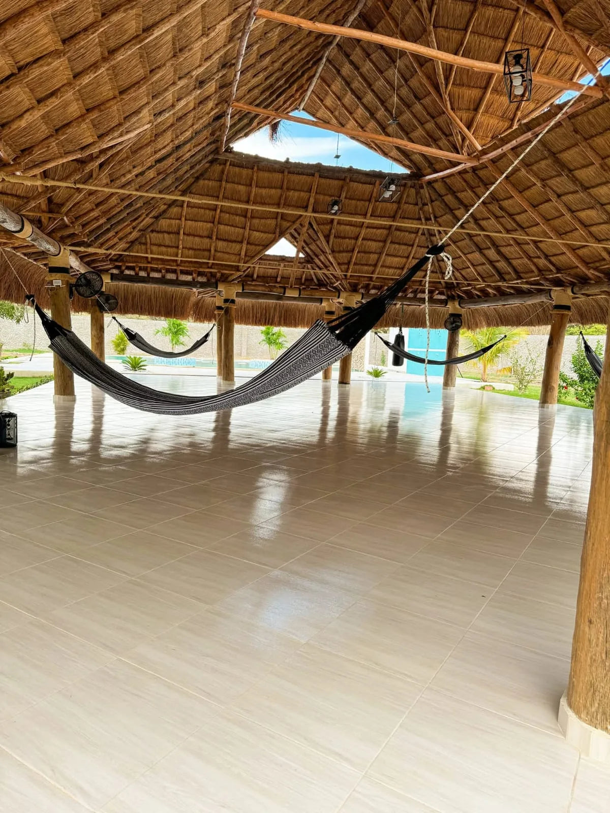 Vista amplia del kiosco de palma con hamacas, estructura de madera y piso cerámico.